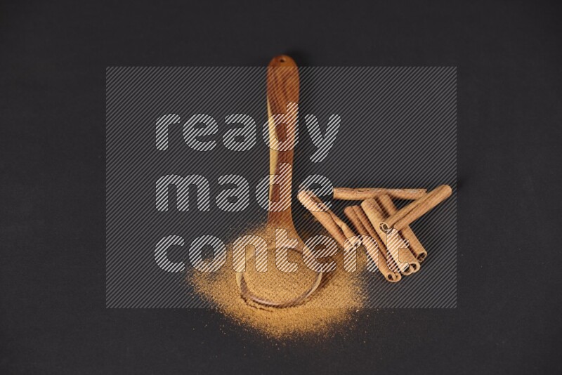 Cinnamon powder in a spoon ladle and spreaded on the floor beside it cinnamon sticks on the floor on black background in different angles