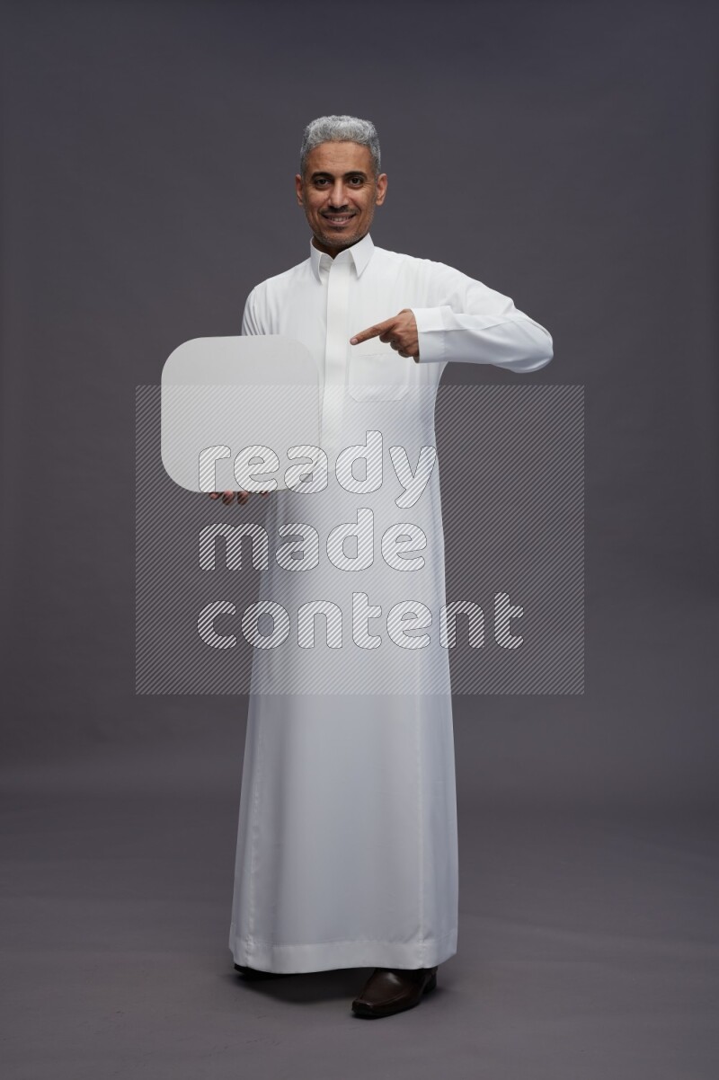 Saudi man wearing thob standing holding social media sign on gray background