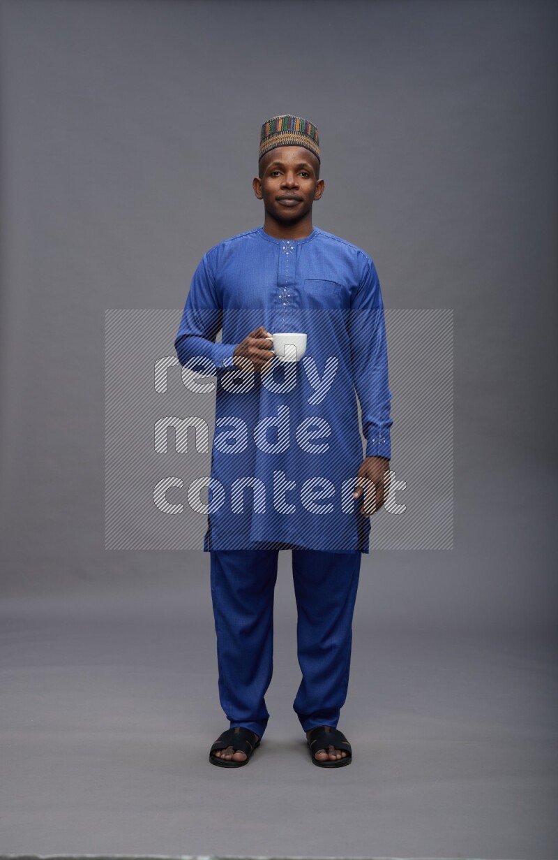Man wearing Nigerian outfit standing holding mug on gray background