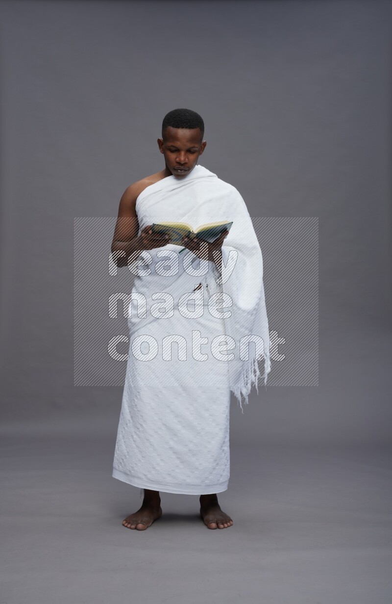 A man wearing Ehram Standing reading quran on gray background