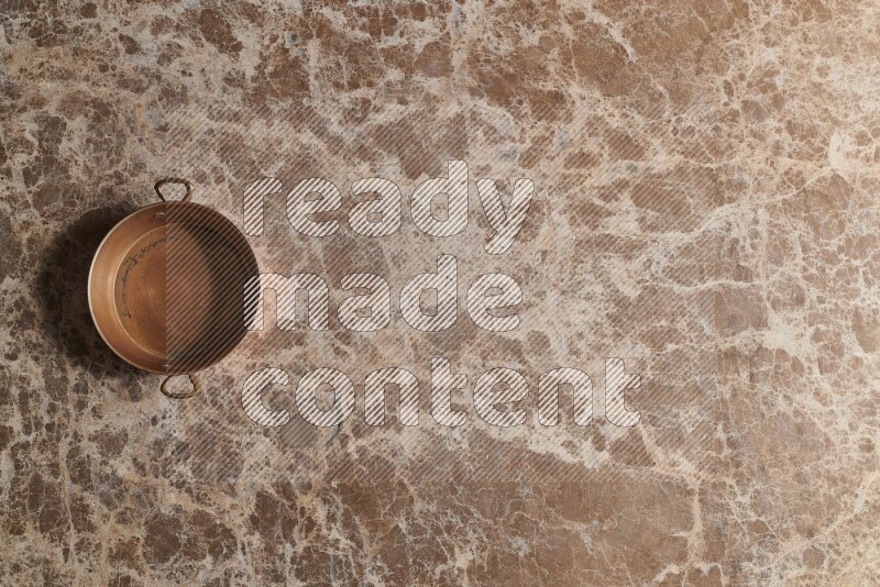 A small copper pan on beige marble background
