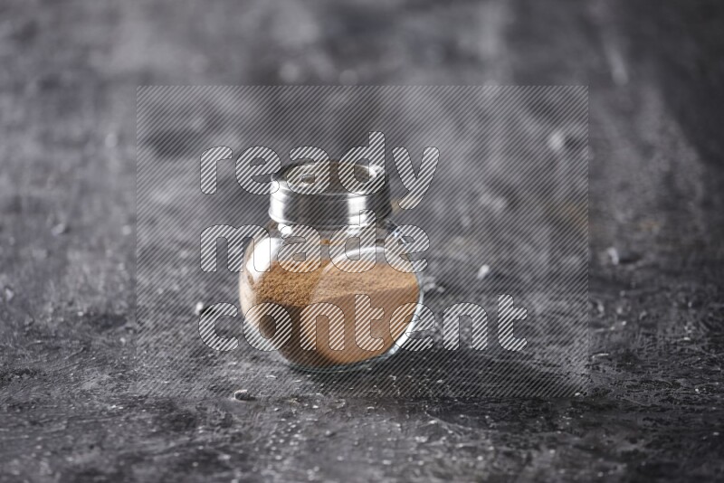 Herbal glass jar full of cinnamon powder on a textured black background