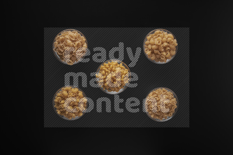 Different pasta types in 5 glass bowls on black background