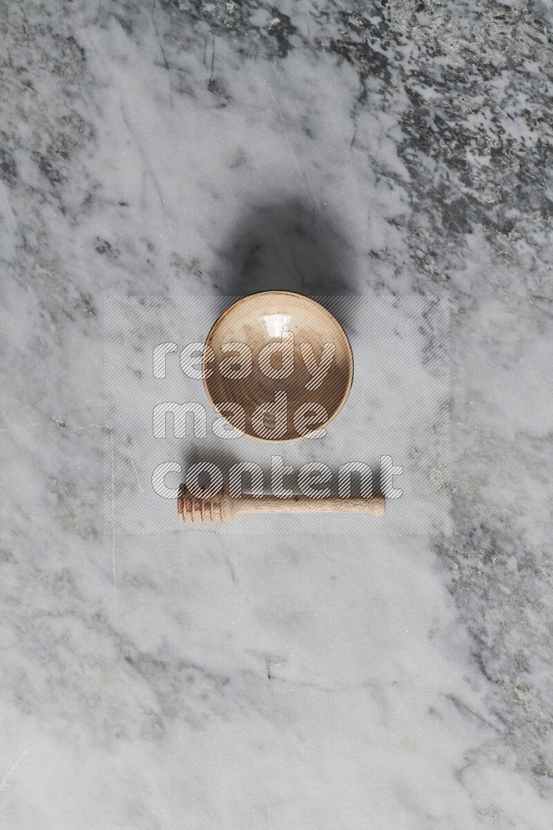 Beige pottery bowl with wooden honey dipper on the side on grey marble background