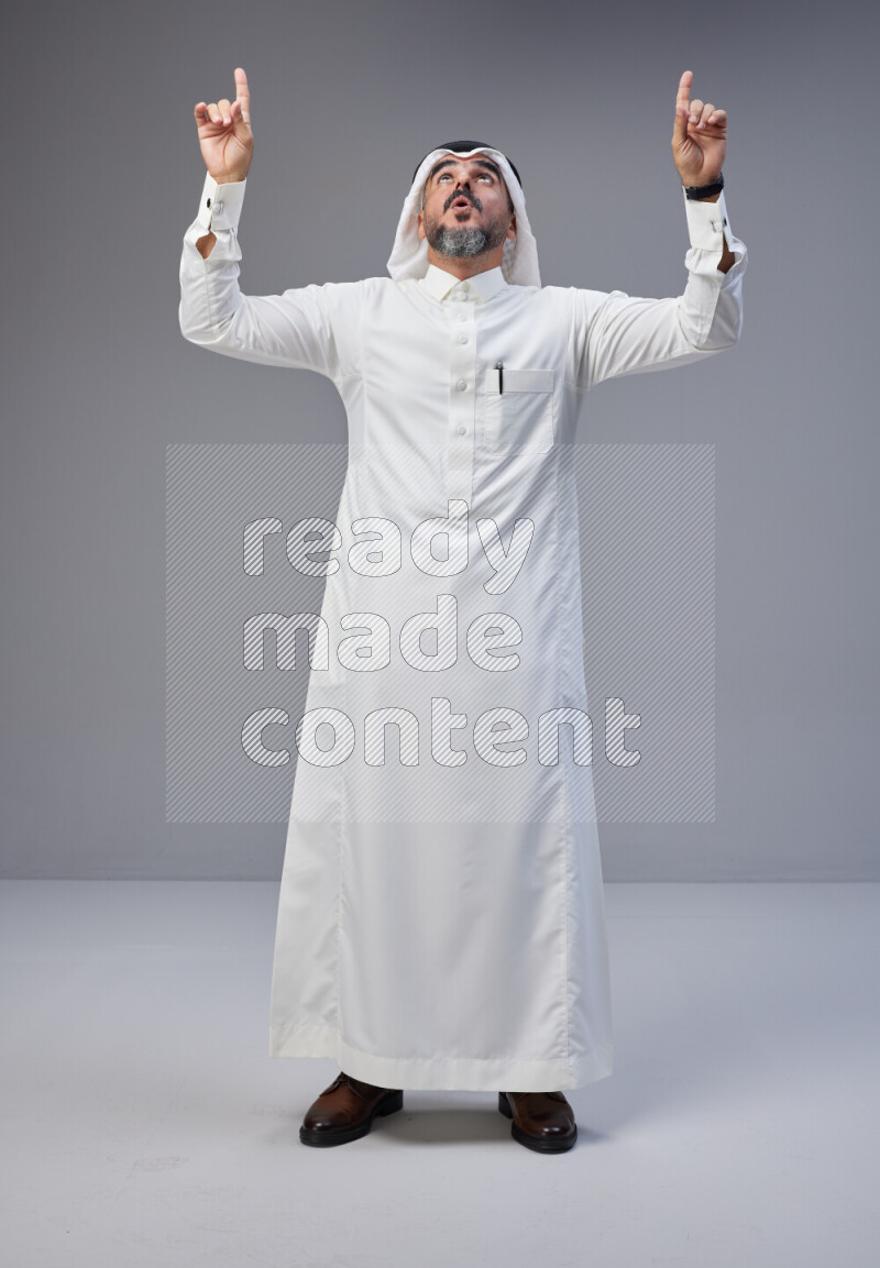 Saudi man Wearing Thob and white Shomag standing interacting with the camera on Gray background