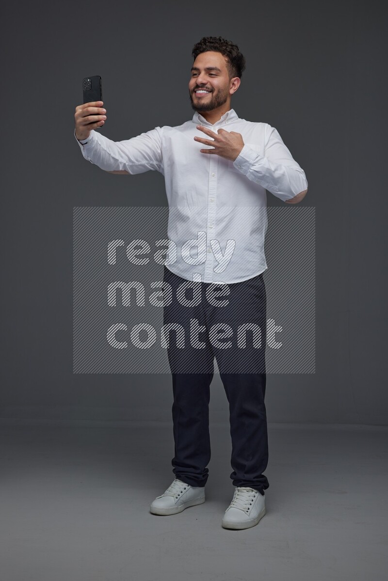 A man wearing smart casual and taking selfie with his phone eye level on a gray background