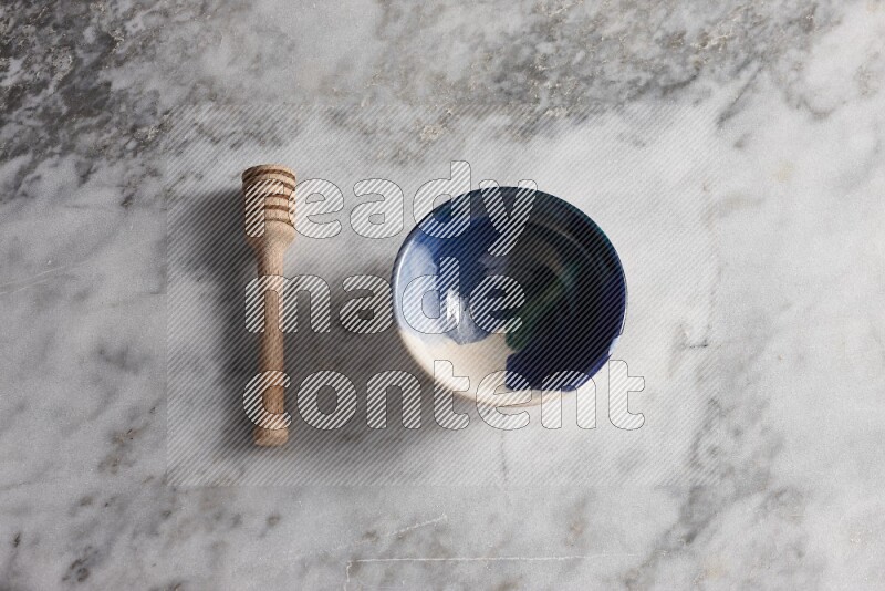 Multicolored pottery bowl with wooden honey dipper on the side on grey marble background