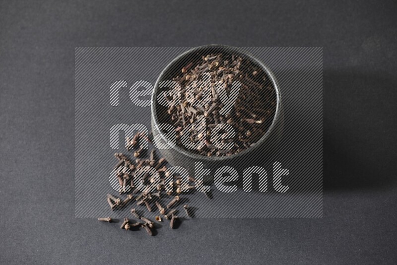 A black pottery bowl full of cloves on a black flooring