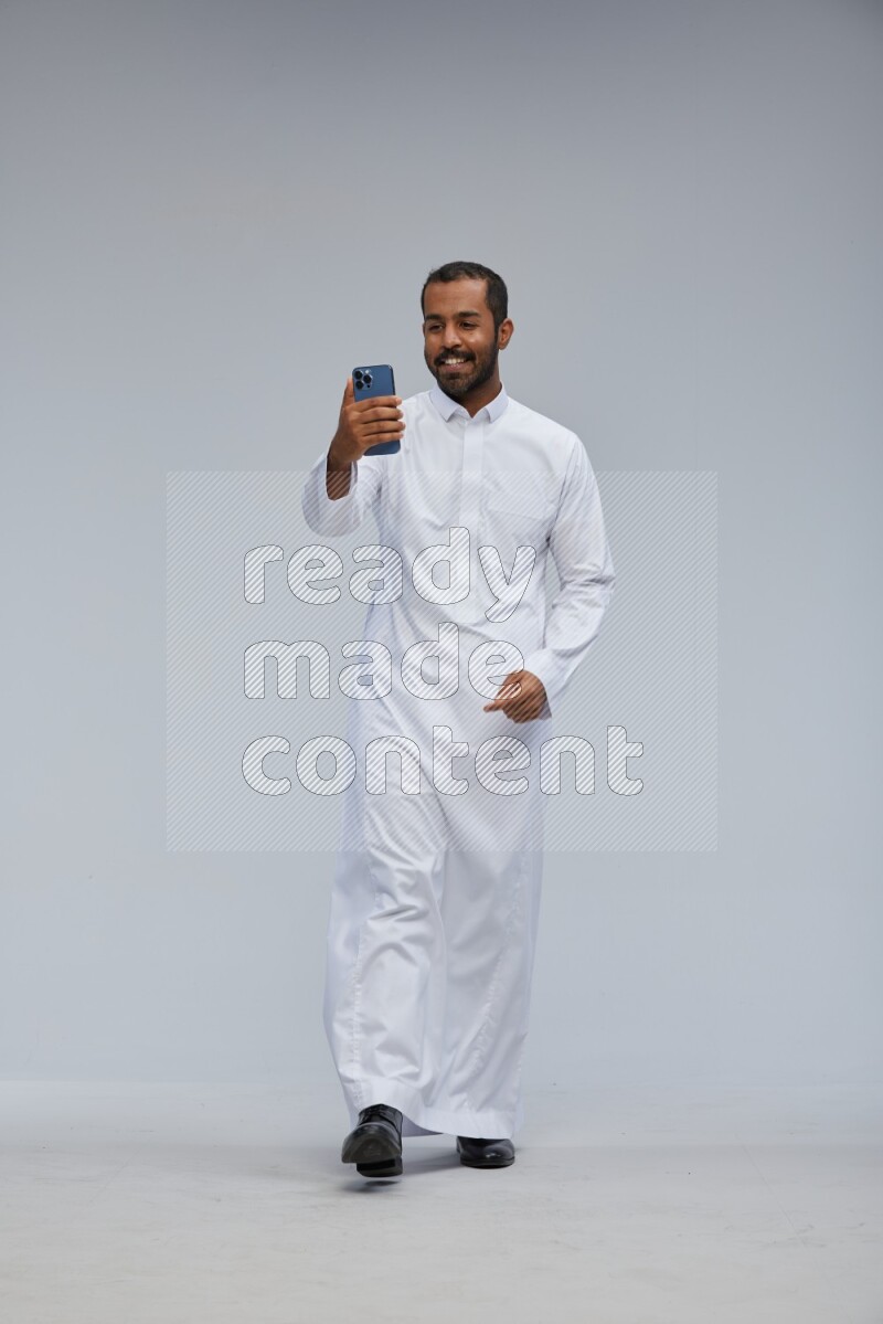 Saudi man wearing Thob standing taking selfie on Gray background