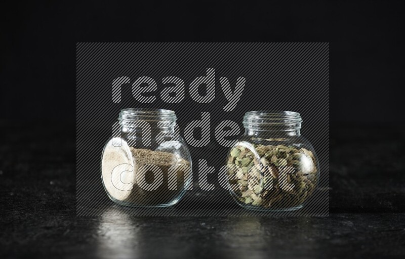 وعاءان زجاجيان ممتلئان ببودرة الهيل وحبوب الهيل على خلفية سوداء