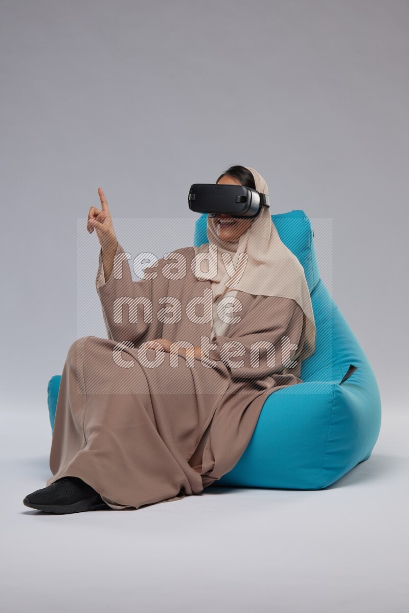 A Saudi woman sitting on a blue beanbag and gaming with VR