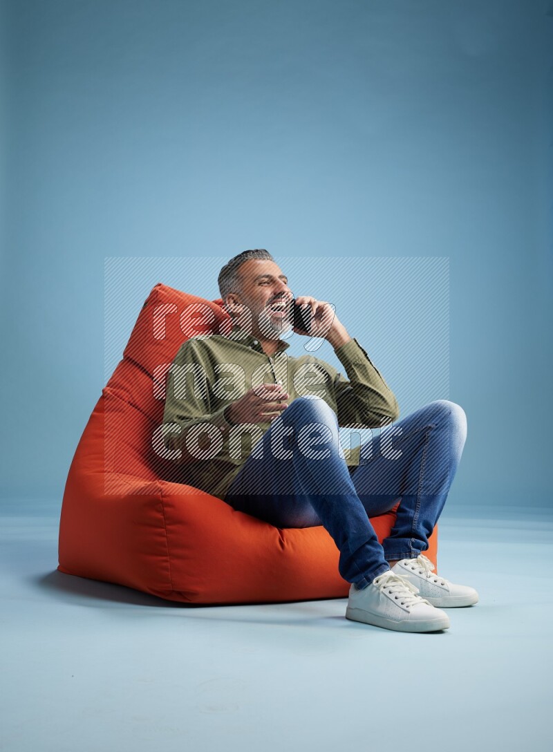 A man sitting on an orange beanbag and talking on the phone