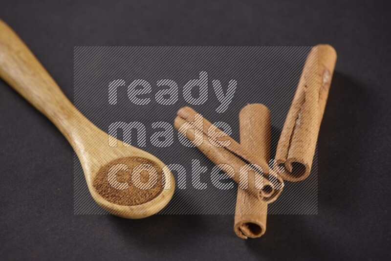 3 Cinnamon sticks stacked beside a wooden spoon full of cinnamon powder on black background in different angles