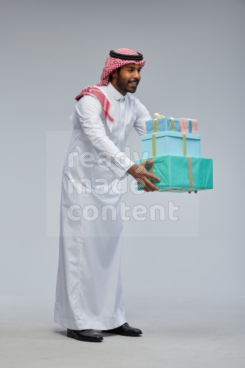 Saudi man Wearing Thob and shomag standing holding gift box on Gray background