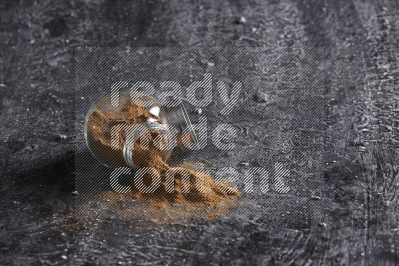 Flipped herbal glass jar full of cinnamon powder on textured black background