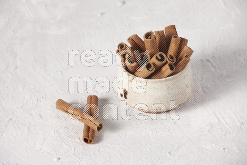 Cinnamon sticks in a beige bowl on a white background