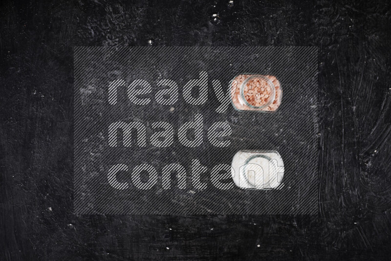 2 وعاء زجاجي احدهمها ممتلئ بملح الهيمالايا الخشن والأخر بملح البحر الخشن على خلفية سوداء