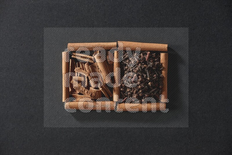 مربعان من أعواد القرفة ممتلئان بالقرنفل وقطع القرفة علي خلفية سوداء