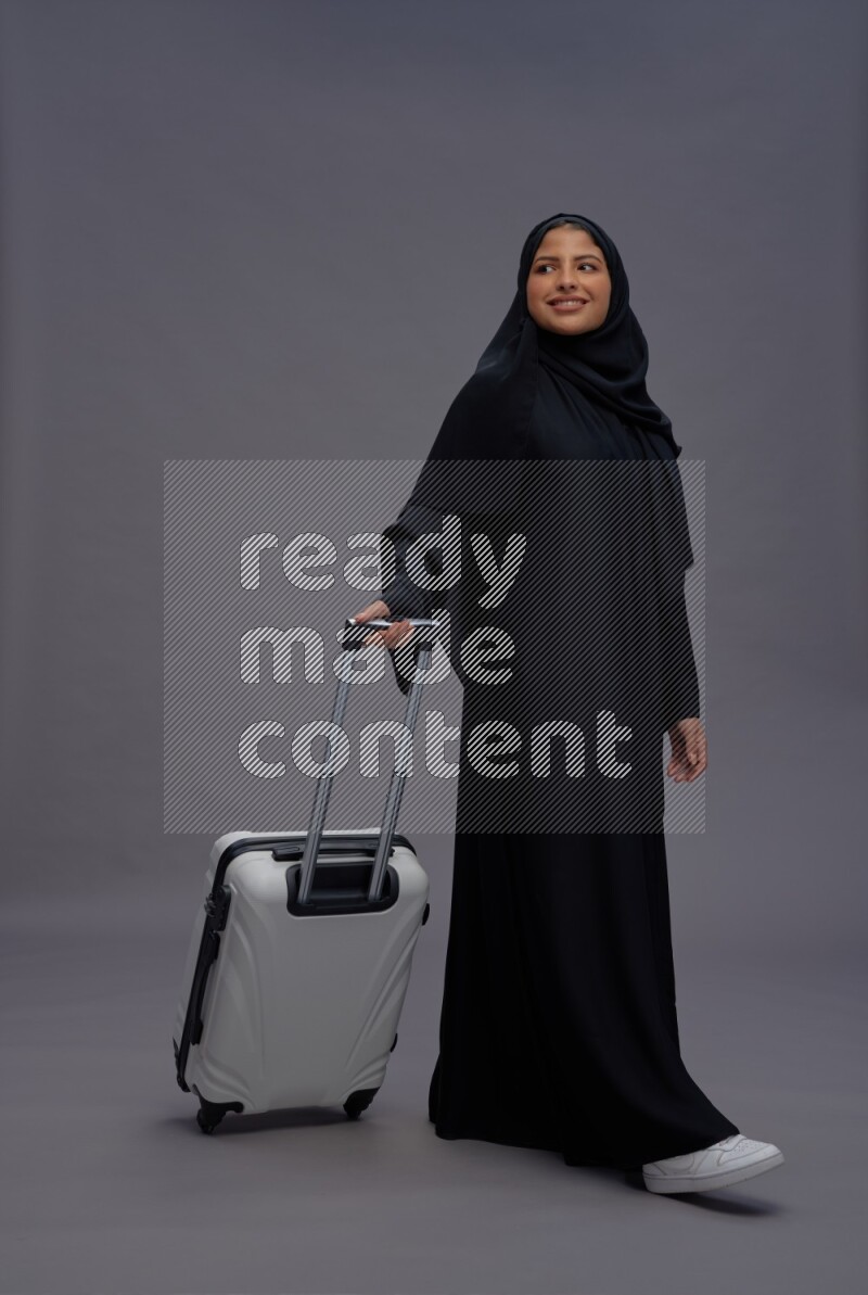 Saudi woman wearing Abaya standing holding bag on gray background
