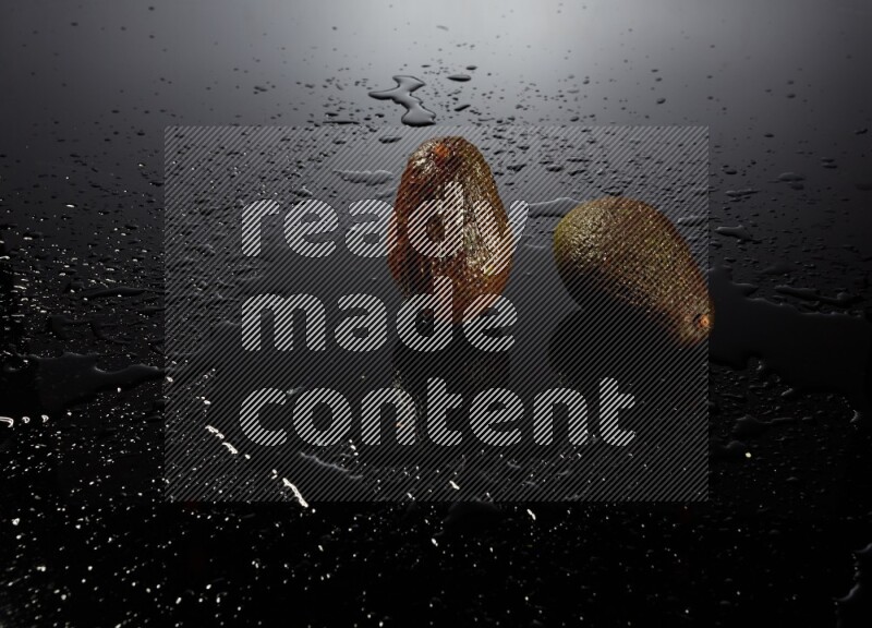 A whole avocado on black background with water drops.