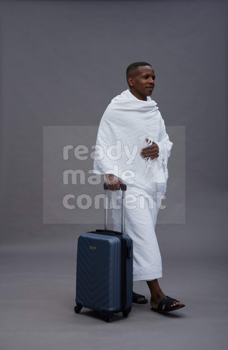 A man wearing Ehram Standing holding traveling bag on gray background