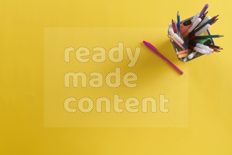 Pens, pencils and school supplies in a metal pen holder on yellow background