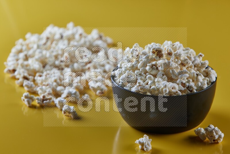 A black ceramic bowl full of popcorn with popcorn beside it on a yellow background in different angles
