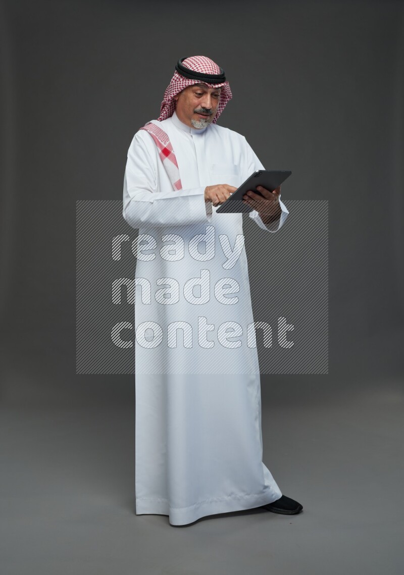 Saudi man with shomag Standing working on tablet on gray background