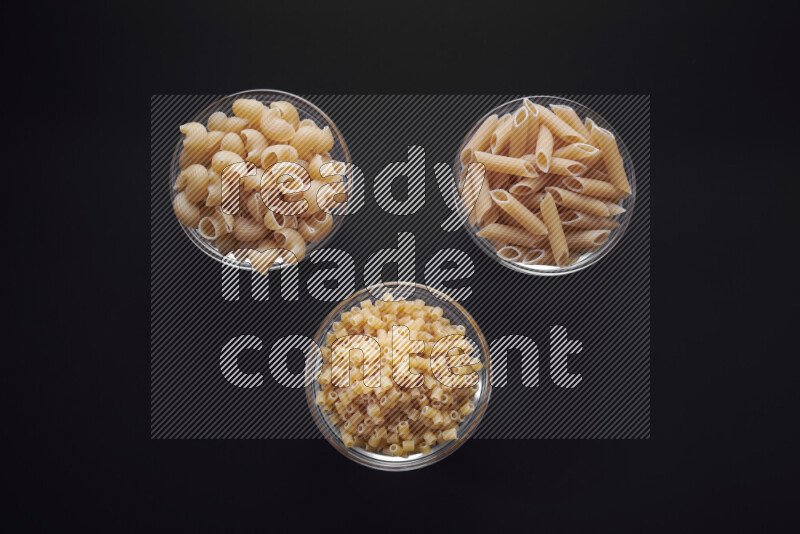 Different pasta types in glass bowls on black background