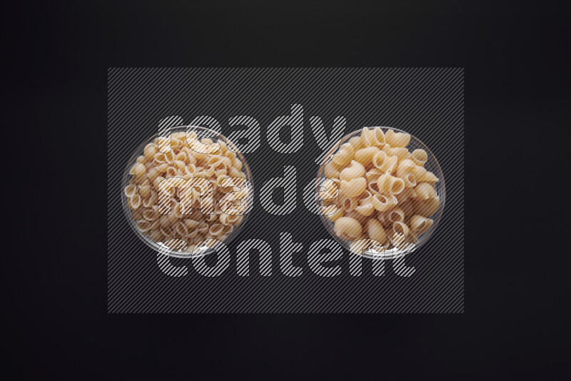 Different pasta types in glass bowls on black background