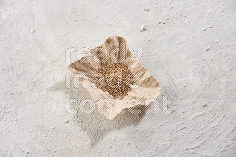 A crumpled piece of paper full of mustard seeds on a textured white flooring