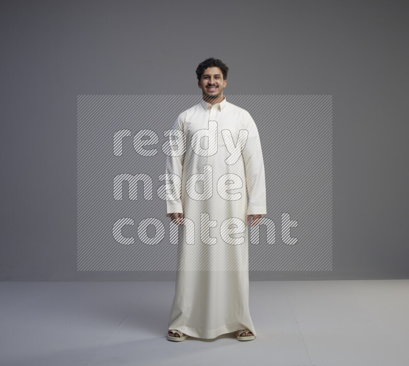 A Saudi man standing wearing thob interacting with the camera on gray background
