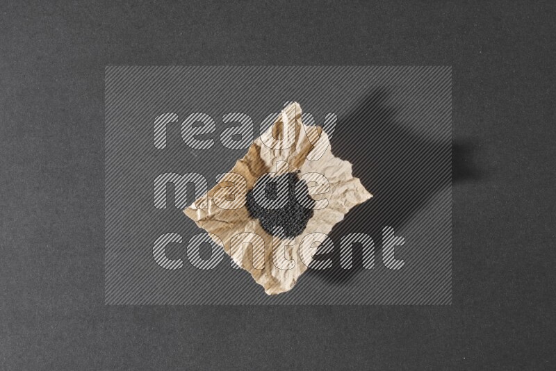 A crumpled piece of paper full of black seeds on a black flooring