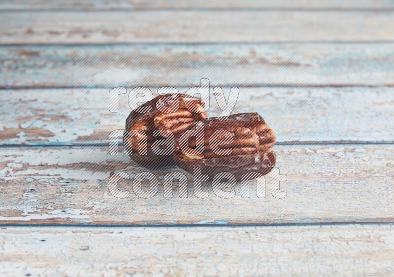 two pecan stuffed madjoul dates on a light blue wooden background