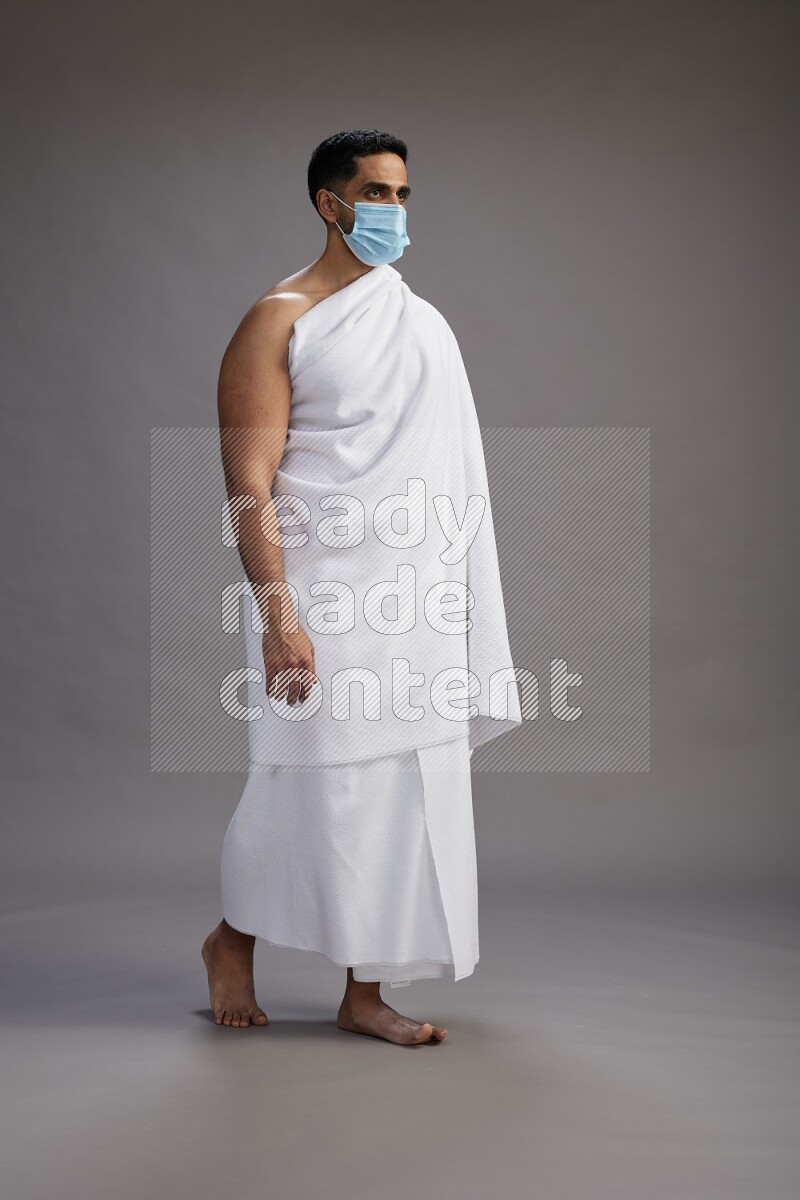 A man wearing Ehram with face mask Standing Interacting with the camera on gray background