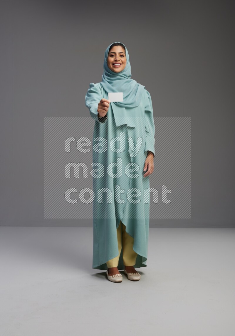 Saudi Woman wearing Abaya standing holding ATM card on Gray background