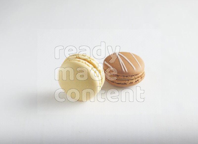 45º Shot of of two assorted Brown Irish Cream, and Yellow Vanilla macarons on white background