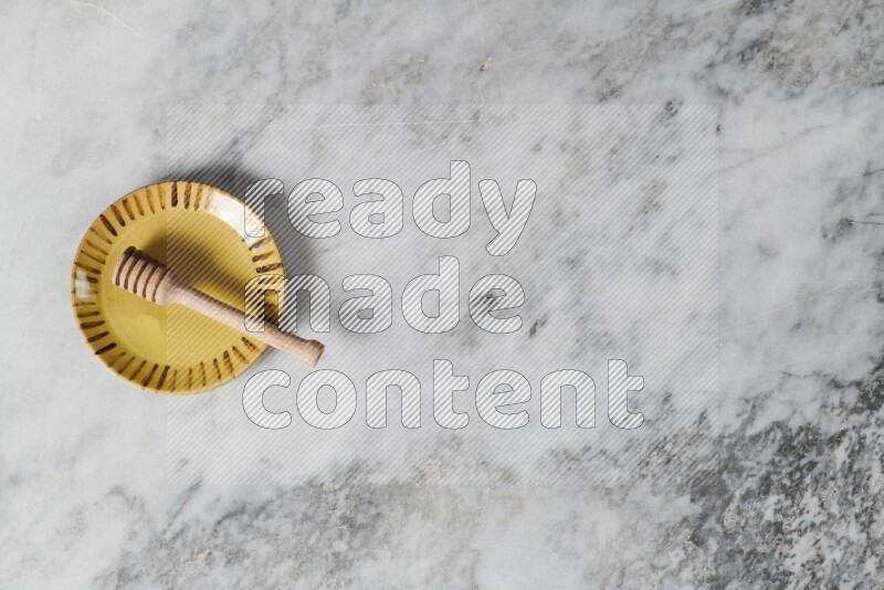 طبق فخاري متعدد الألوان مع ملعقة عسل خشبية بداخله على خلفية من الرخام الرمادي