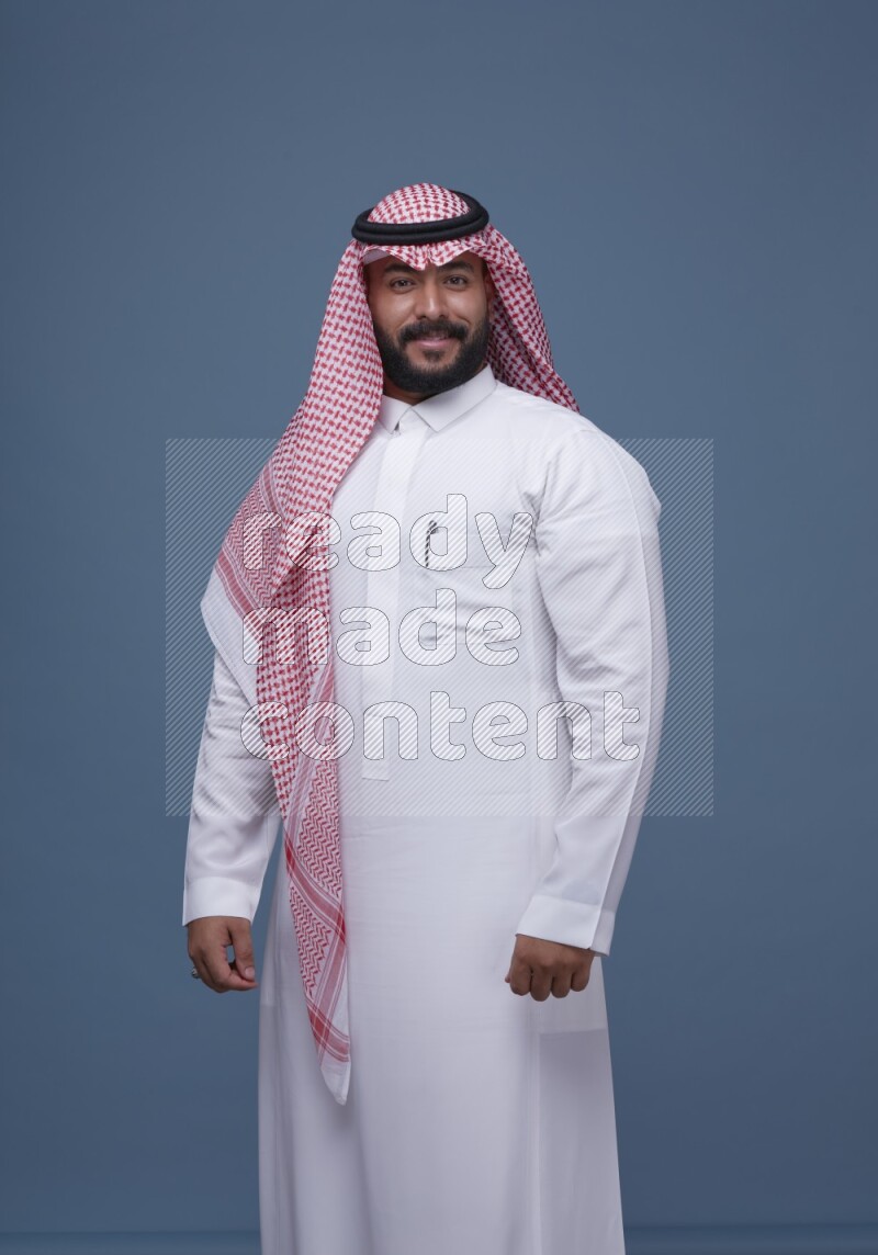 A Saudi man posing on blue background wearing Thob and Shomag