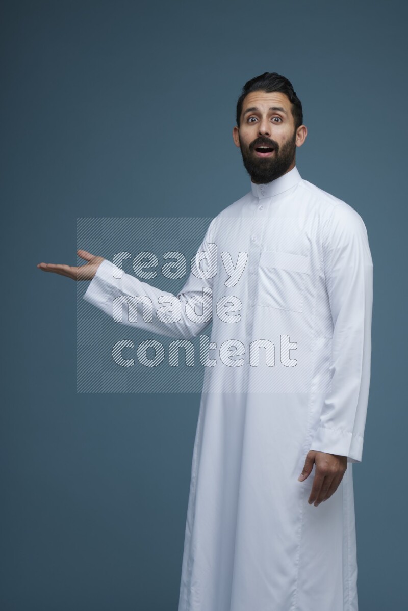 A man pointing in a blue background wearing Saudi Thob