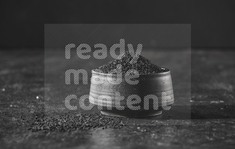 وعاء فخاري أسود ممتلئ ببذور حبة البركة علي خلفية سوداء