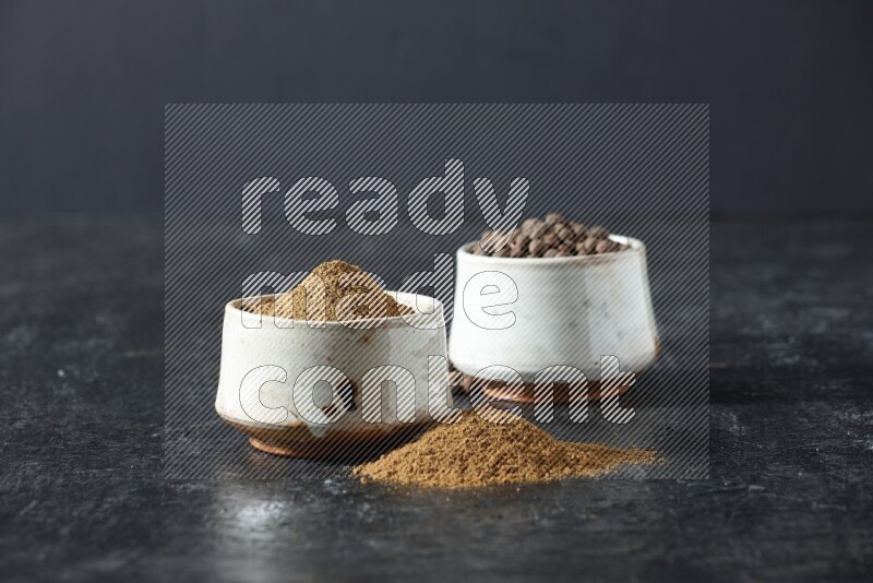 2 beige bowls, one full of allspice powder and the other full of whole balls and both spread on a textured black flooring