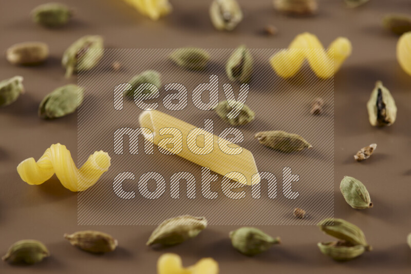 Raw pasta with different ingredients such as cherry tomatoes, garlic, onions, red chilis, black pepper, white pepper, bay laurel leaves, rosemary and cardamom on beige background