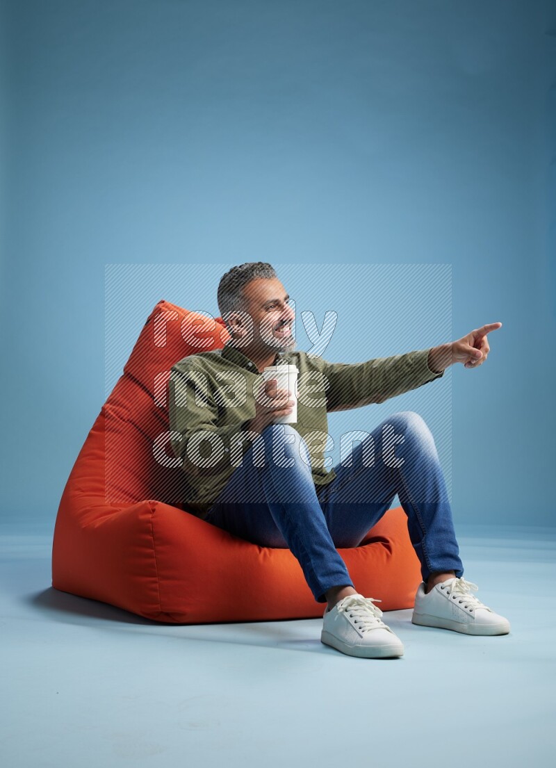 A man sitting on an orange beanbag and drinking coffee