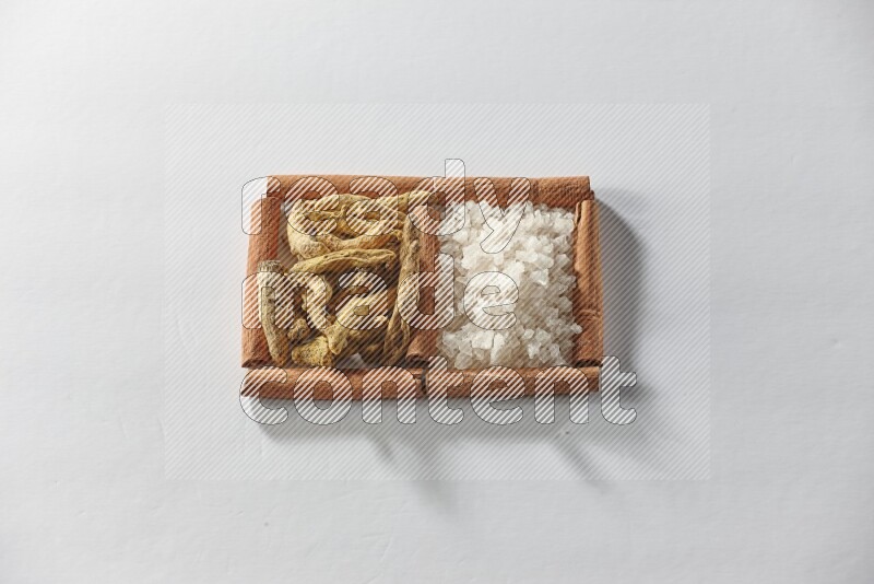 مربعان من أعواد القرفة ممتلئان بأصابع الكركم والملح الأبيض علي خلفية بيضاء