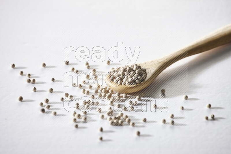 A wooden spoon full of white pepper beads on white flooring