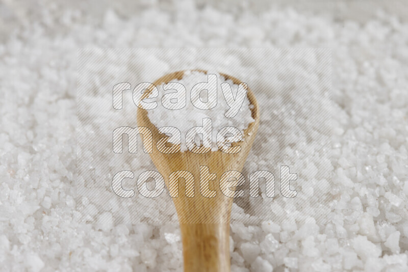 A wooden spoon full of white salt on white background