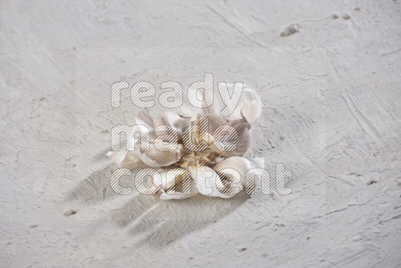 A cracked garlic bulb showing the cloves inside it on a white flooring