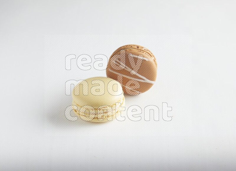 45º Shot of of two assorted Brown Irish Cream, and Yellow Vanilla macarons on white background