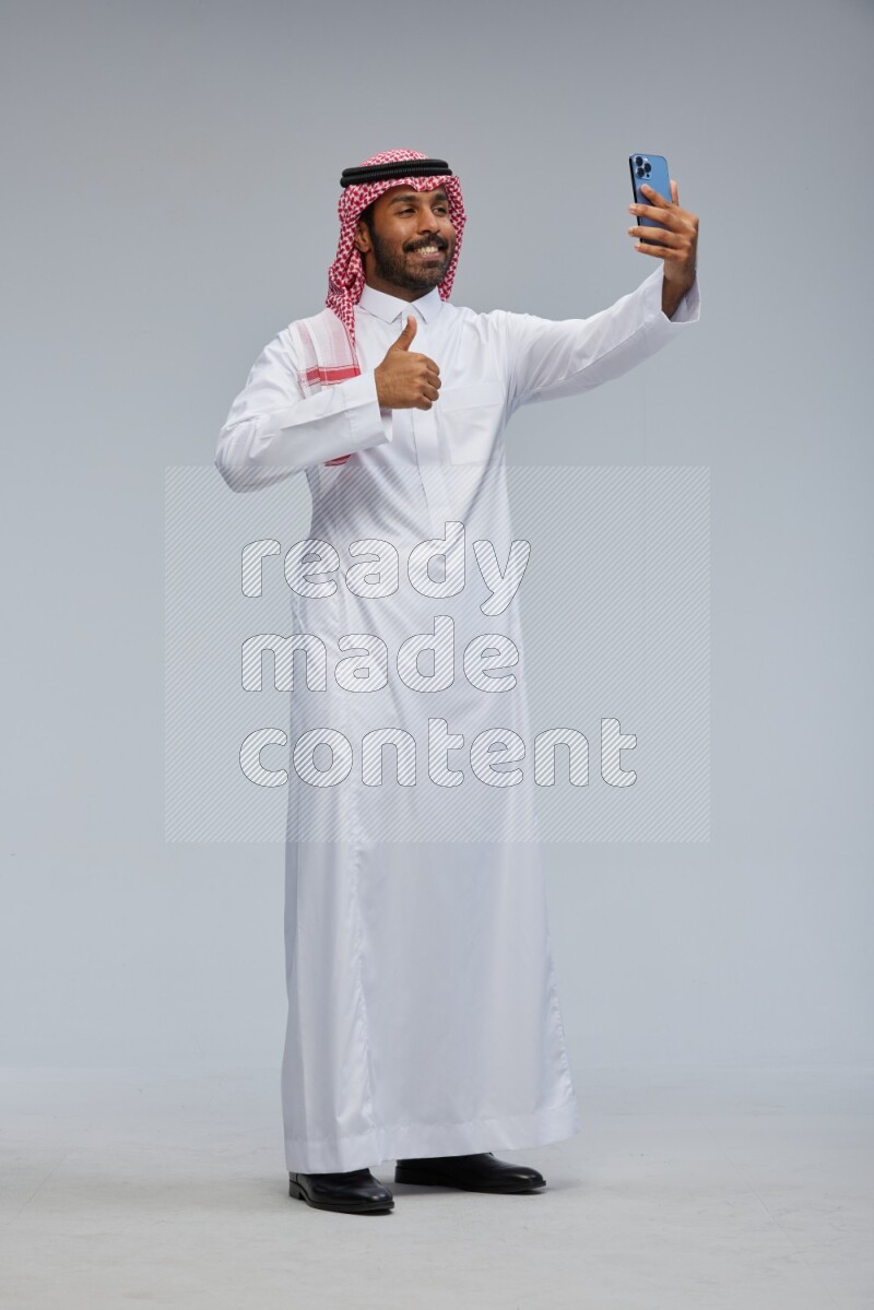 Saudi man Wearing Thob and shomag standing taking selfie on Gray background
